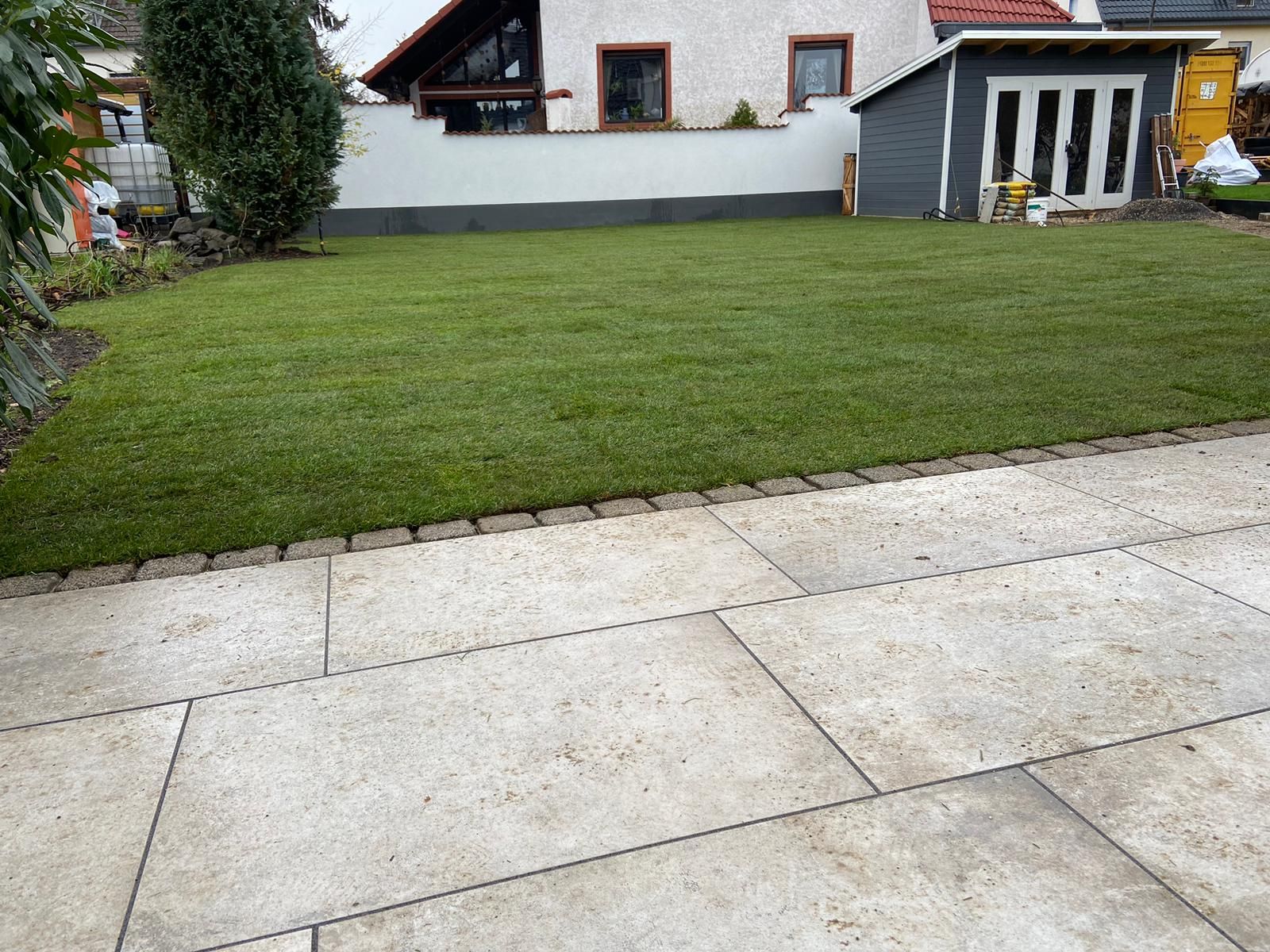 Terrasse aus hellen großformatigen Platten mit sauberem Übergang zum Rasen