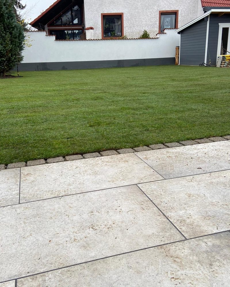 Frisch verlegter Rollrasen hinter einer neuen Terrasse aus großen Platten